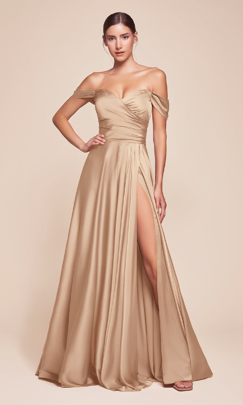 A woman stands gracefully against a beige background, wearing the Ladivine 7493-1—an off-the-shoulder, champagne-hued long prom dress with a high slit and floor-length A-line silhouette.