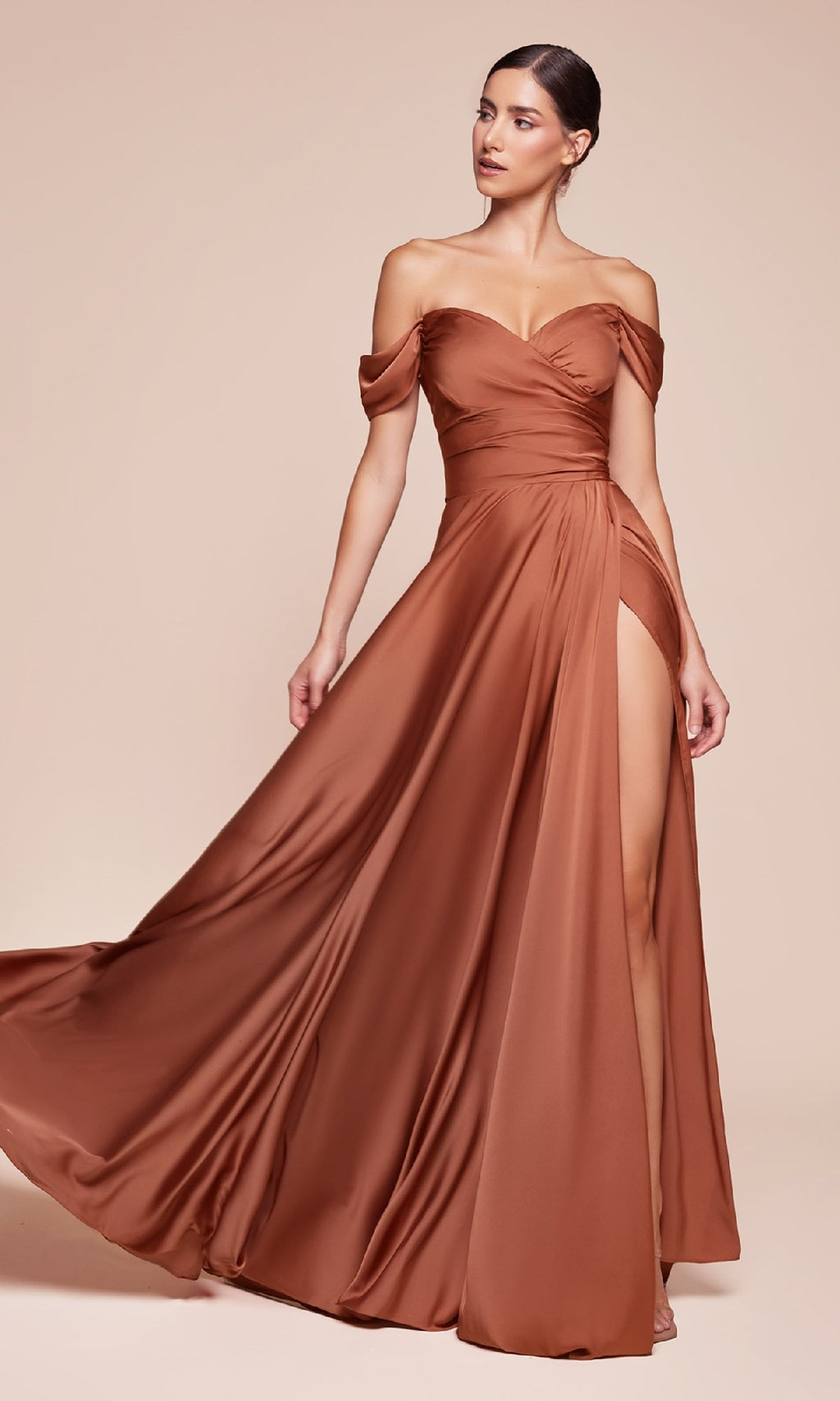 A woman poses against a beige background in the Empire-Waist Plus-Size Long Prom Dress 7493C, featuring copper satin fabric, an off-the-shoulder neckline, ruched bodice, and a high slit.