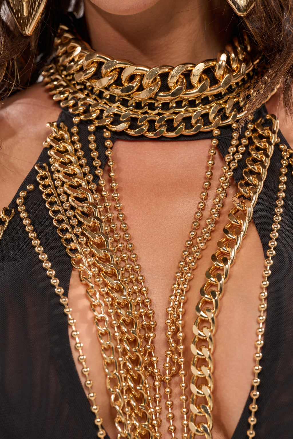 A close-up of a person wearing the STAND OUT CHAIN MINI DRESS, featuring layered gold-tone chains draped over their chest and neck for a bold, statement look.