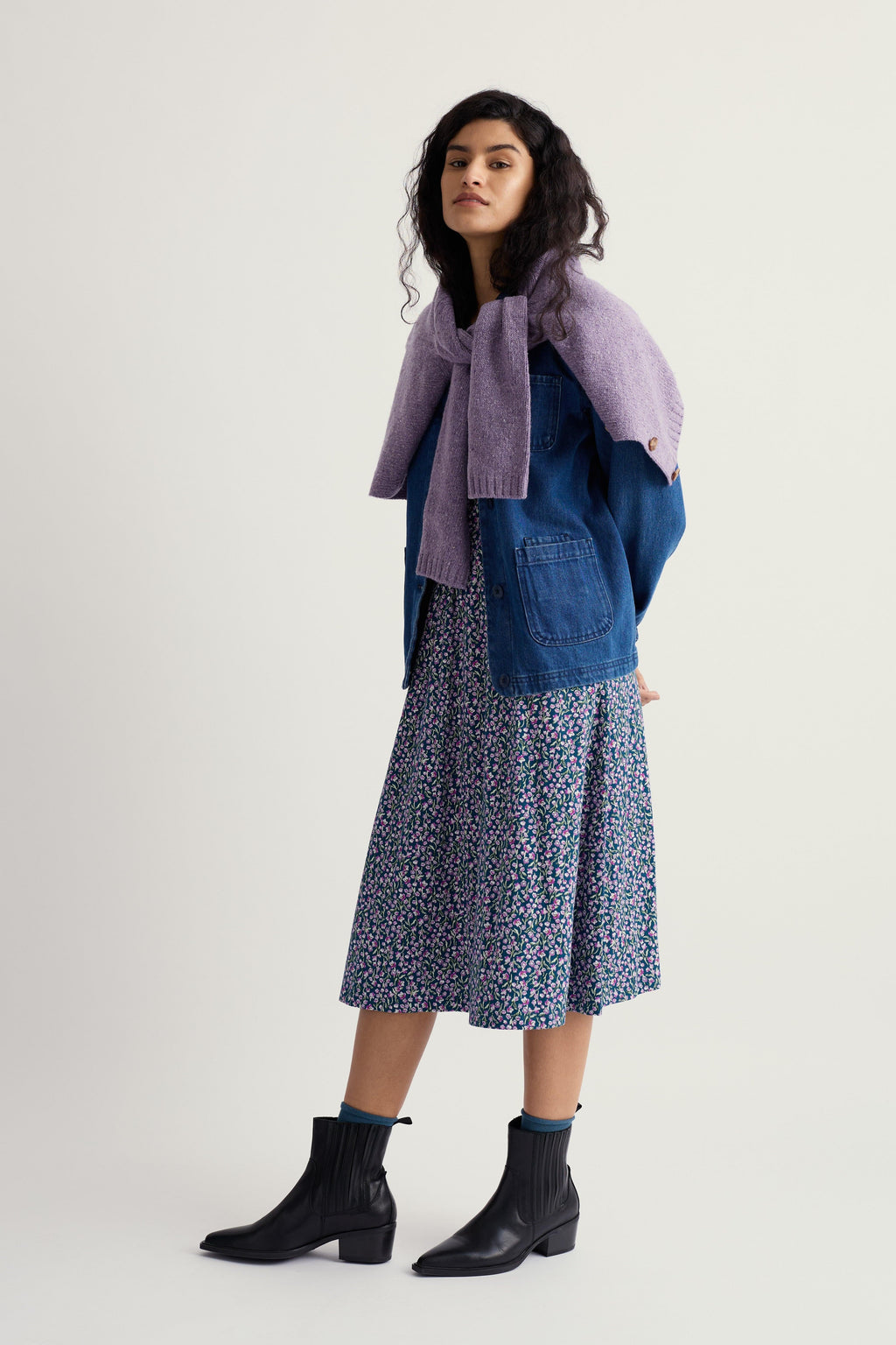 Woman wearing a floral organic cotton dress and a denim jacket on a white background
